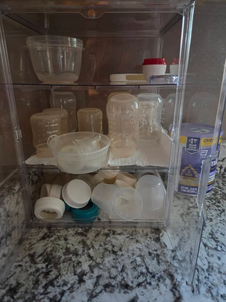 Our clear kitchen cabinet holding bottle bodies, loose collars, caps and a bowl of nipples