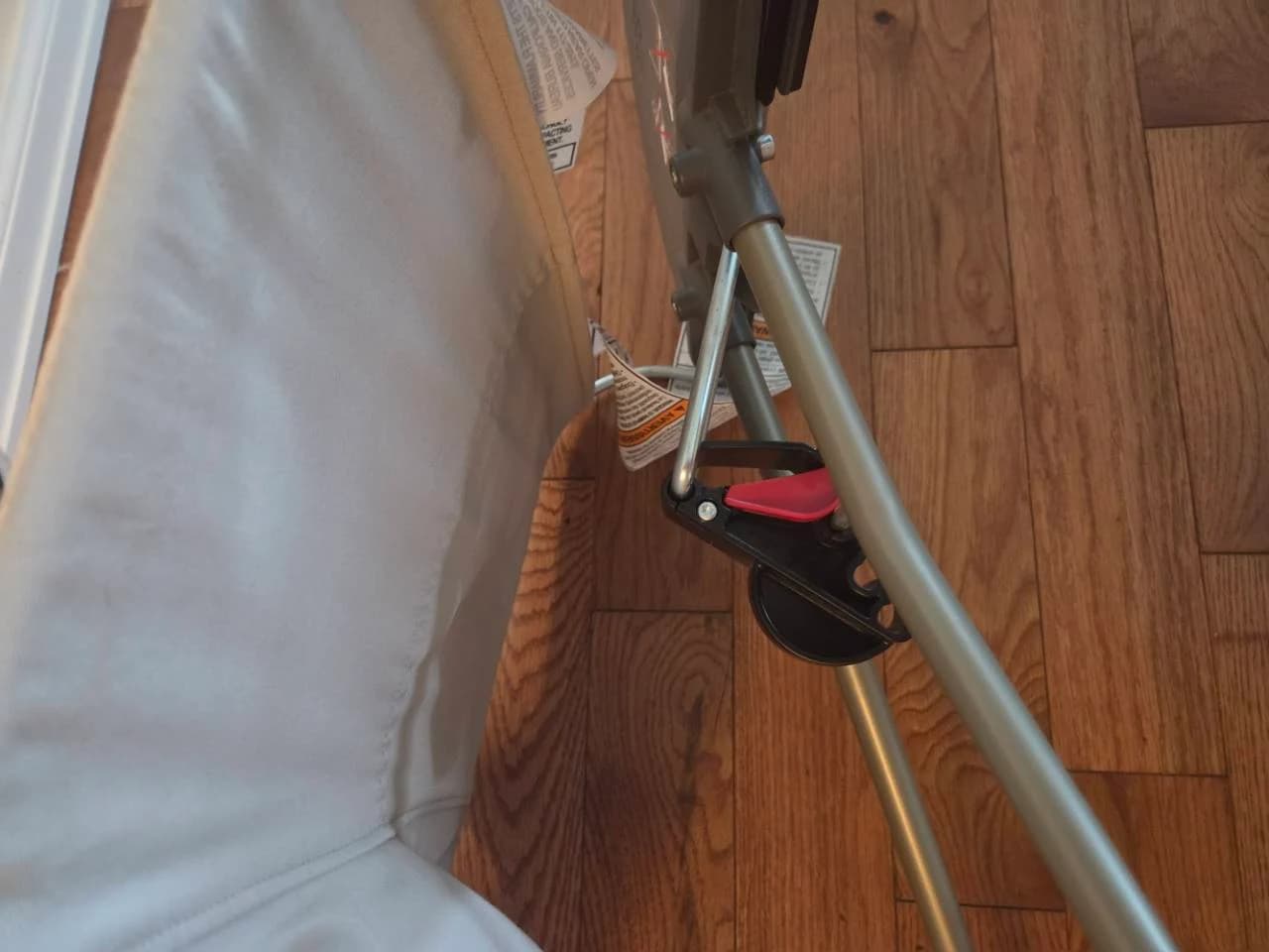 Close-up beneath our BabyBjörn bouncer showing the red and black adjustment assembly beside the metal frame