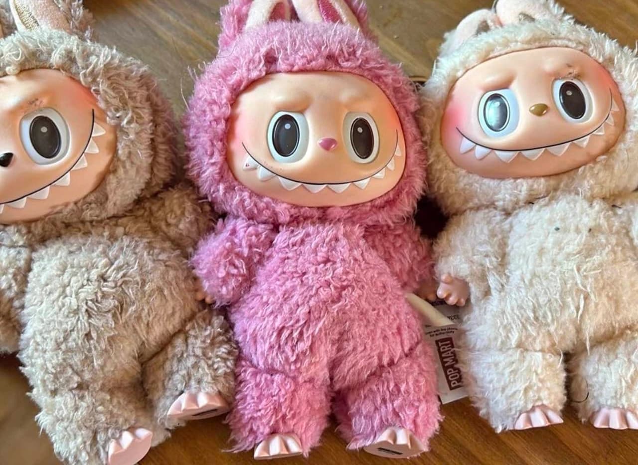 Brown, pink and cream Labubu plush dolls on a wooden surface