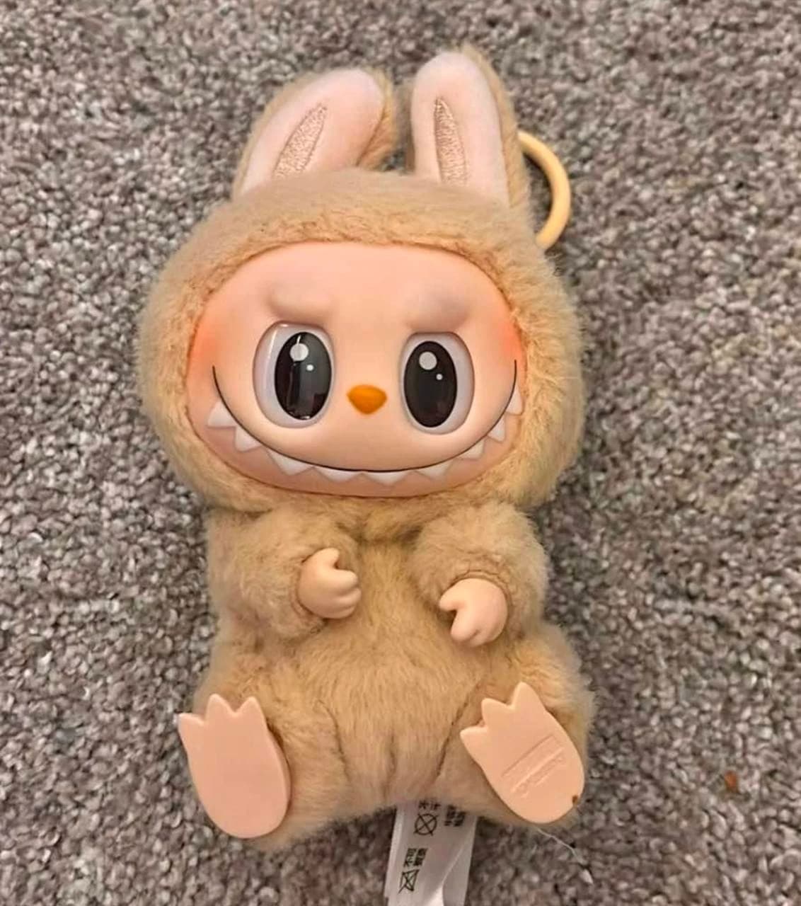 Tan Labubu plush in a seated pose on carpet with its feet facing forward