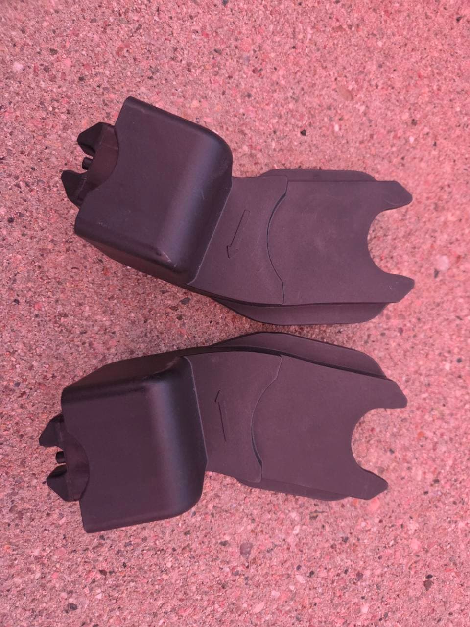 The two black adapter pieces for our Clek car seat laid out on pavement
