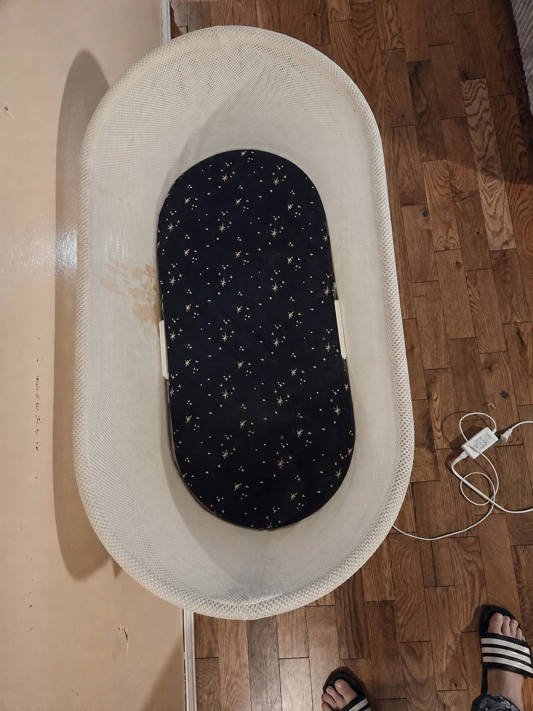 Overhead view of our empty SNOO with a dark star-patterned sheet and a brown coffee stain on the left mesh wall